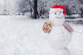 Happy snowman wearing Santa hat in snowy winter park at Christmas season outdoors holding presents. Winter activities Royalty Free Stock Photo