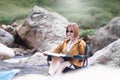 Happy solo woman traveller reading map while sitting on chair at waterfall