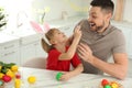 Happy son with bunny ears headband and his father having fun while painting Easter egg in kitchen Royalty Free Stock Photo