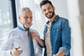 Happy son helping cheerful retired father tying blue tie