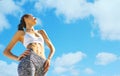 Happy smiling sports woman with tanned fit body and tattoo posing against blue sky with clouds, bottom view. Royalty Free Stock Photo