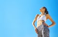 Happy smiling sports woman with tanned fit body and tattoo posing against blue sky, bottom view. Royalty Free Stock Photo