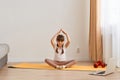 Happy sporty Caucasian little girl meditating in living room, healthy child with raised arms sitting on the floor yoga mat in