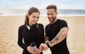 Happy sporty couple resting after jogging by seaside, checking smartwatch fitness tracker, enjoying training outdoors Royalty Free Stock Photo