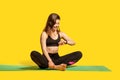 Happy sporty girl in tight sportswear sitting on gym mat, looking time, checking pulse in fitness tracker Royalty Free Stock Photo