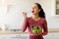 Happy sporty woman eats fresh salad in the kitchen indoor Royalty Free Stock Photo