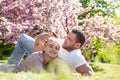 Happy spring couple in love having fun. Two young people relaxing in sakura flowers. Smiling lovers relaxing in park