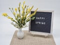Happy Spring written on a black and white letter board with white font and a yellow flower arrangement in a white glass vase