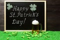 Happy St. Patricks Day chalk lettering on blackboard, mug of beer and shamrock leaves on green grass, dark wooden planks Royalty Free Stock Photo