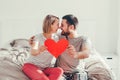 Happy strong marriage. Happy funny couple in love holding red paper heart. Heterosexual family man and woman sitting on bed in Royalty Free Stock Photo