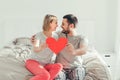 Happy strong marriage. Happy funny couple in love holding red paper heart. Heterosexual family man and woman sitting on bed in Royalty Free Stock Photo