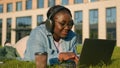 Happy student girl African American woman female relaxing on lawn lying on green grass listening music in headphones Royalty Free Stock Photo