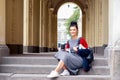 Happy student girl is holding paper cup while sitting on outdoor stairs Royalty Free Stock Photo