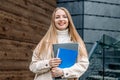 Happy student girl holds folders notebooks books in hands smiles against the background of a modern university building Royalty Free Stock Photo