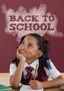 Happy student girl at table against red blackboard with back to school text Royalty Free Stock Photo