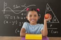 Happy student girl at table holding an apple against grey blackboard with education and school graph Royalty Free Stock Photo