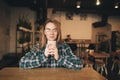 Happy student girl wearing glasses and a shirt, sitting in a cafe holding a cup of coffee in his hands, looking into the camera Royalty Free Stock Photo