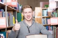 Happy student with pile books showing thumbs up in college library Royalty Free Stock Photo