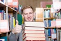 Happy student with pile books showing thumbs up in college library Royalty Free Stock Photo