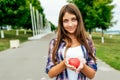 Happy student student girl holding a toy heart summer city. Free space text. Background of road green trees. Concept of