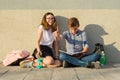 Happy students on campus pathway, teenagers sit on the gray wall, read textbooks, drink water, look at the tablet. Boy is holding Royalty Free Stock Photo