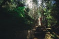 Happy stylish couple newlyweds in the green forest on summer day. bride in long white dress and groom in red suit are hugging.