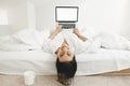 Happy stylish girl  lying on bed with laptop with blank screen and smiling in white modern room. Young cheerful woman shopping Royalty Free Stock Photo