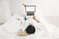 Happy stylish girl lying on bed with laptop with blank screen in white modern room. Young woman looking at empty display, shopping Royalty Free Stock Photo