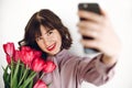 Happy stylish girl making selfie with pink tulips and gift box w