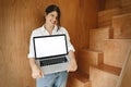 Happy stylish girl showing laptop with empty screen, standing at wooden stairs in modern room. Young business woman working online Royalty Free Stock Photo