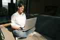 Happy stylish girl sitting on floor with laptop in sunny light. Young woman smiling, holding laptop, shopping online or working Royalty Free Stock Photo