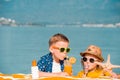 Happy stylish little boy and toddler girl drinking orange juice and eatting ice cream on tropical beach resort. Family Royalty Free Stock Photo