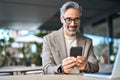 Smiling mature business man using phone sitting outside office. Candid photo. Royalty Free Stock Photo