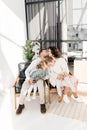 Happy stylish parents sitting on chairs with beautiful kids, spending weekends at home. Loving husband kissing lovely Royalty Free Stock Photo