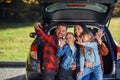 Happy stylish parents with their cute lovely children are making funny selfie on smart phone while sitting in the trunk Royalty Free Stock Photo