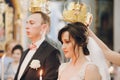 Happy stylish wedding couple holding candles with light under golden crowns during holy matrimony in church. Bride and groom Royalty Free Stock Photo