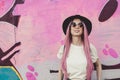 Happy stylish young hipster woman with long pink hair, hat and sunglasses on the street.