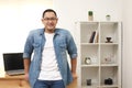 Happy succesful young Asian entrepreneur smiling at camera confidently in his home office studio