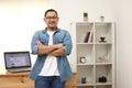 Happy succesful young Asian entrepreneur smiling at camera confidently in his home office studio