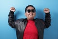 Happy success fat Asian boy wearing leather jacket and sunglasses shows winning gesture Royalty Free Stock Photo