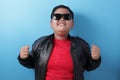 Happy success fat Asian boy wearing leather jacket and sunglasses shows winning gesture Royalty Free Stock Photo