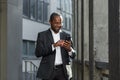 Happy successful African American businessman boss walking outside office building, manager holding smartphone reading Royalty Free Stock Photo