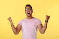 Happy successful african american young man screaming with hands up over yellow background.