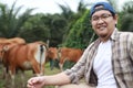 Happy successful Asian farmer looking at camera and smiling, with domesticated cow ox cattle grazing in the background, Royalty Free Stock Photo