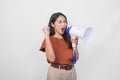 Happy successful Asian woman wearing a brown shirt raising clenched fist while shouting and screaming loud using megaphone speaker Royalty Free Stock Photo