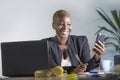 Happy successful black afro american woman in business jacket working cheerful at office laptop taking notes using mobile phone Royalty Free Stock Photo