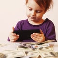 Happy successful business baby girl holding a smartphone in front of bunch of money (humorous picture) Royalty Free Stock Photo