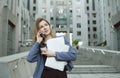 Happy successful businesswoman calling with cell telephone outside office building holding laptop, documents, coffee.Female Royalty Free Stock Photo