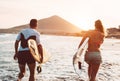 Happy surfer couple running with surfboards along the sea shore - Sporty people having fun going to surf together at sunset Royalty Free Stock Photo