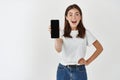 Happy and surprised brunette woman showing blank smartphone screen at camera, standing over white background